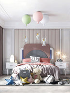 Green, pink and white Clérachic balloon lights with astronauts above a bed heaped with soft toys and star cushions.