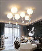 Six white Clérachic balloon lights with astronauts cluster on a ceiling above a spaceship bed and a window with sheer curtains.