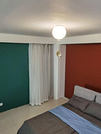 One white Clérachic balloon light with a small moon-shaped ornament, above a bed between green and rust-red walls.