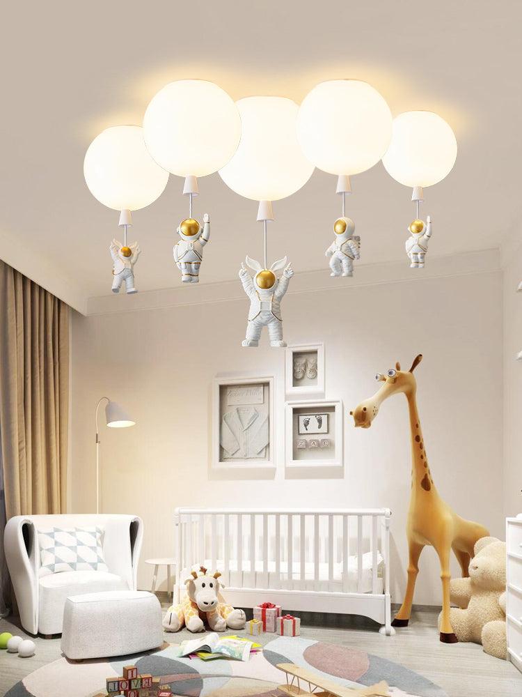 Five white Clérachic balloon lights with astronauts above a nursery with a white cot and a tall toy giraffe.
