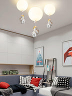 Three white Clérachic balloon lights with astronauts in a white-and-grey room with a sofa, cushions and framed posters.
