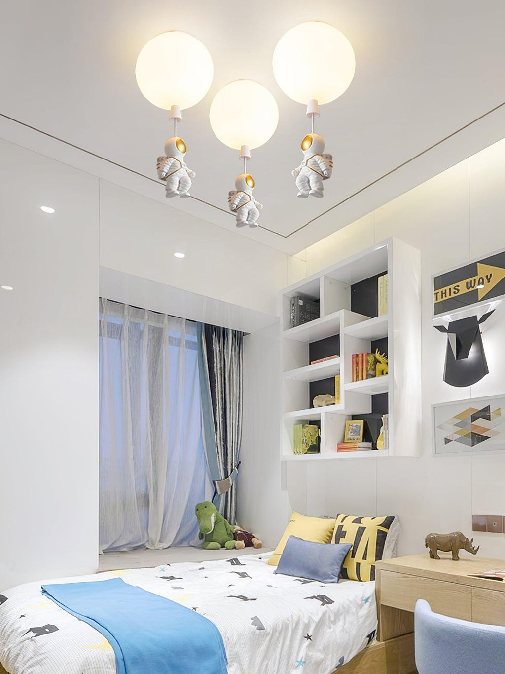 Three white Clérachic balloon lights with astronauts above a bed with a blue throw and a white shelving unit.