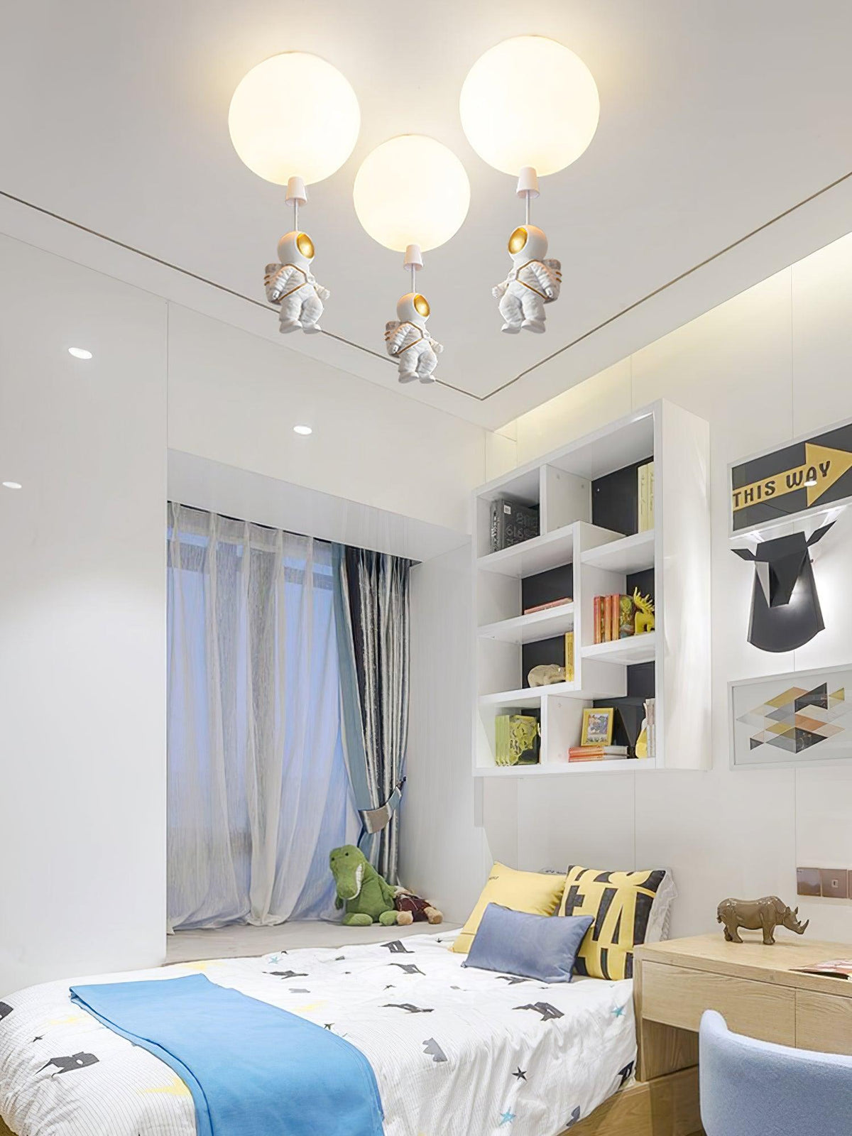 Three white Clérachic balloon lights with astronauts above a bed with a blue throw and a white shelving unit.
