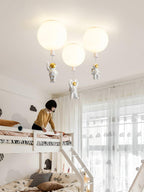 Three white Clérachic balloon lights with astronauts above a white bunk bed, with a woman making the bed beside it.