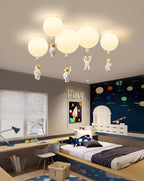 Five white Clérachic balloon lights with astronauts above a play-themed bedroom with a planet-print wall and a raised bed.