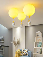 Three yellow Clérachic balloon lights with astronauts in a room with a white house-shaped shelf and a blue chair.