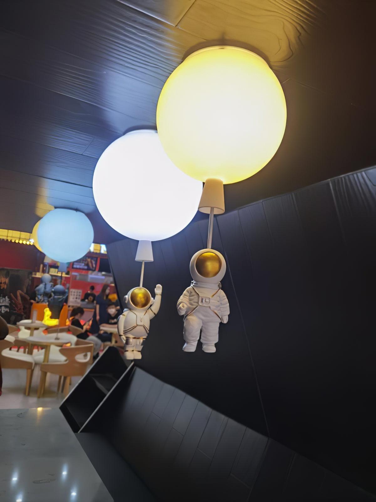 Yellow, white and blue Clérachic balloon lights with astronauts above a café seating area with a dark angled ceiling.