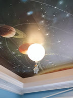 One white Clérachic balloon light with an astronaut under a ceiling printed with planets and stars, in a room with a blue border.