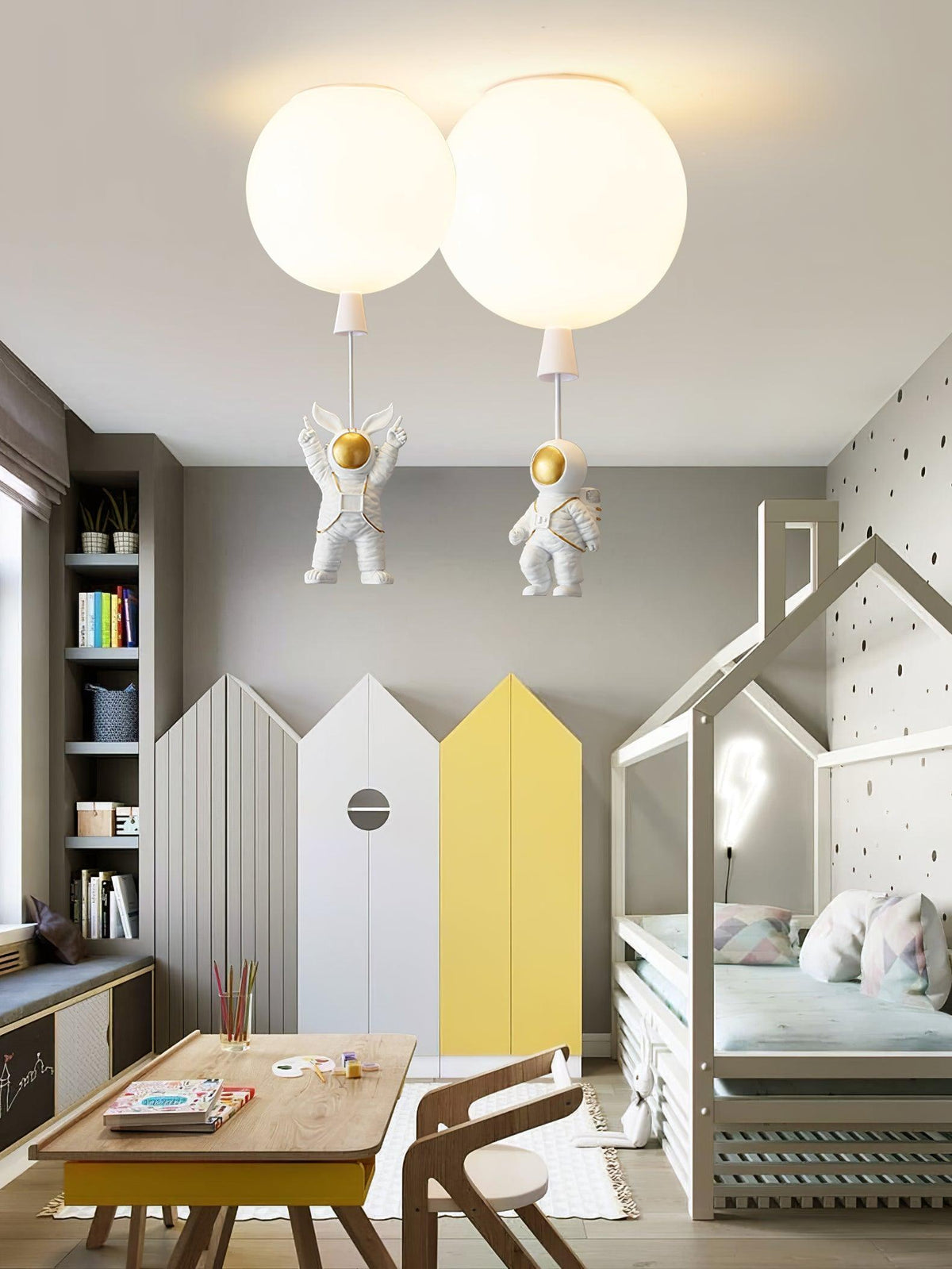 Two white Clérachic balloon lights with astronauts above a child's room with house-shaped wardrobe doors and a wooden table.