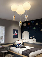Three white Clérachic balloon lights with astronauts above a bed beside a navy planet-print wall and a toy telescope.