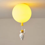 Lit yellow Clérachic balloon ceiling light, the diffuser glowing warmly, with a waving astronaut beneath.