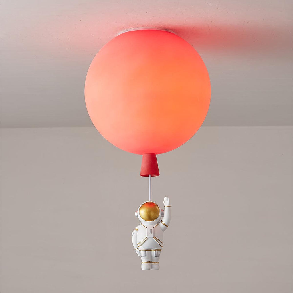 Lit red Clérachic balloon ceiling light, the diffuser glowing orange-red, with a waving astronaut on a cord below.