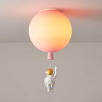 Lit pink Clérachic balloon ceiling light with a peach glow and a waving astronaut on a cord below.