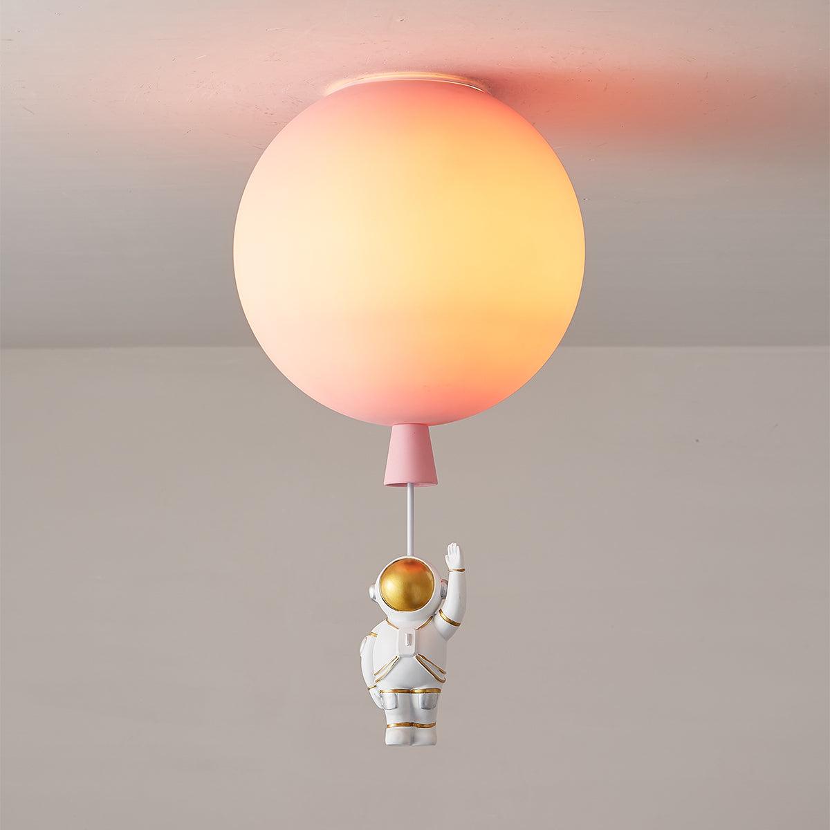 Lit pink Clérachic balloon ceiling light with a peach glow and a waving astronaut on a cord below.