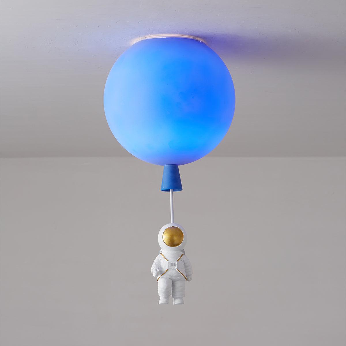 Lit blue Clérachic balloon ceiling light with a deep blue glow and a seated astronaut hanging underneath.