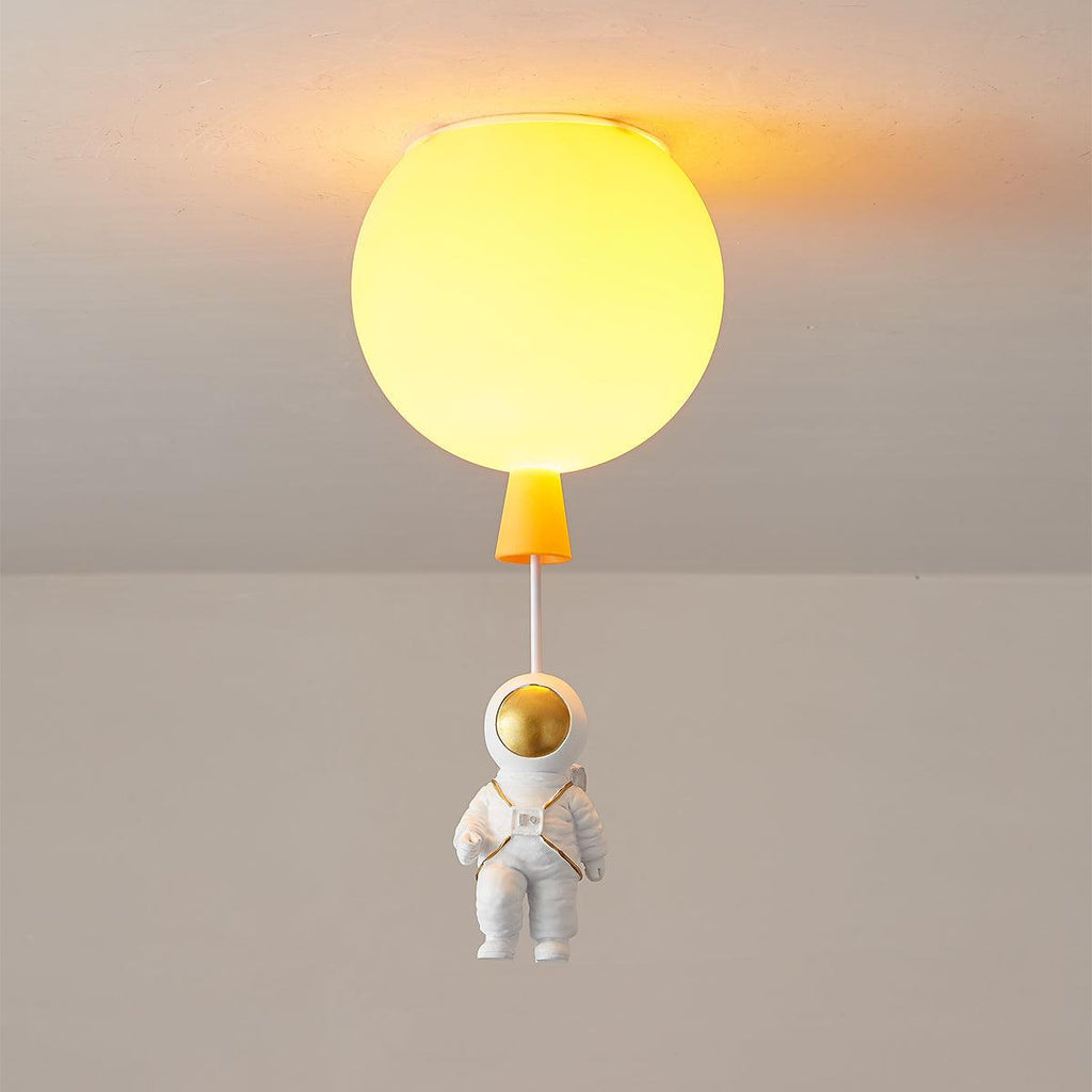 Lit orange Clérachic balloon ceiling light with a warm yellow-orange glow and a seated astronaut on a cord.