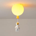 Lit orange Clérachic balloon ceiling light with a warm yellow-orange glow and a seated astronaut on a cord.