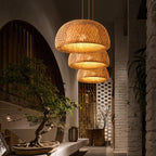 Clérachic three woven bamboo dome pendants at staggered heights, glowing warm in a room with a bonsai and white brick wall.