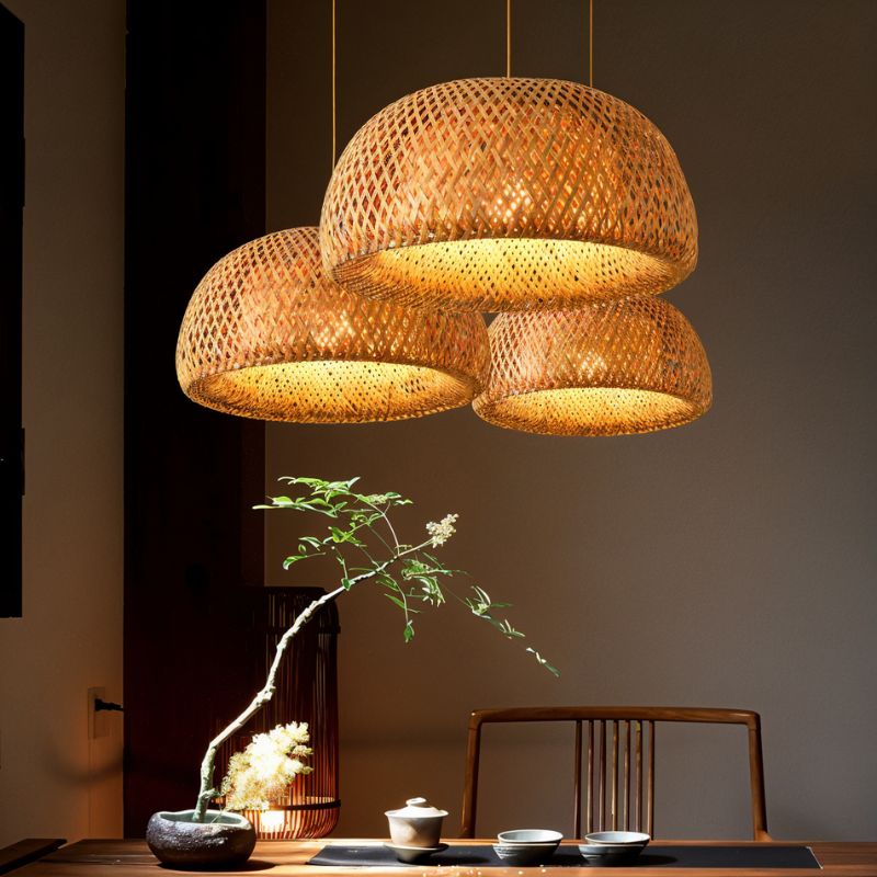Clérachic cluster of three woven bamboo pendants glowing over a wooden table with a tea set and a branch in a stone vase.