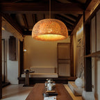 Clérachic large woven bamboo dome pendant hanging in a timber-beamed room with a low sofa, a long wooden table and a tea tray.