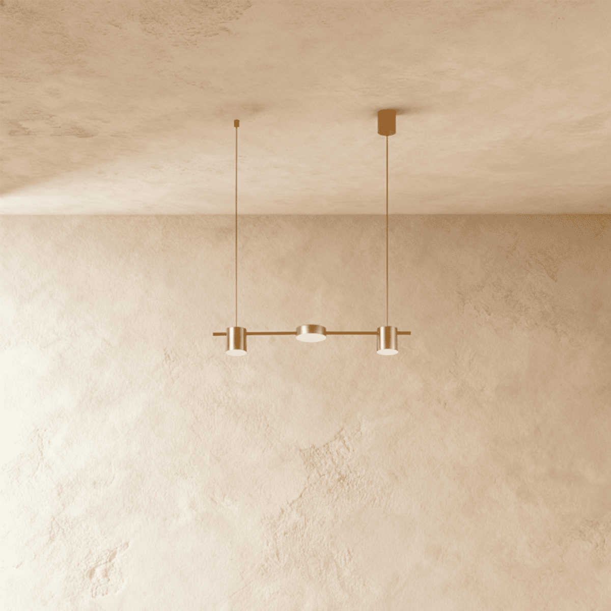 The Clérachic three-head pendant bar in brushed gold, its round LED heads glowing warm white against a plaster wall.