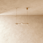 Angled view of the Clérachic gold three-head pendant bar, cylindrical heads glowing warm white beneath a textured ceiling.