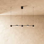 Another angle of the Clérachic black five-head pendant bar, cylindrical heads glowing warm white on fine cables.