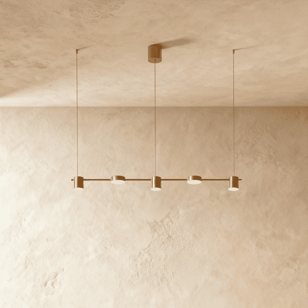 The Clérachic five-head pendant bar in brushed gold, its round LED heads glowing warm white against a plaster wall.