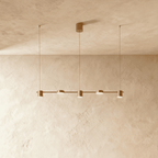 The Clérachic five-head pendant bar in brushed gold, its round LED heads glowing warm white against a plaster wall.