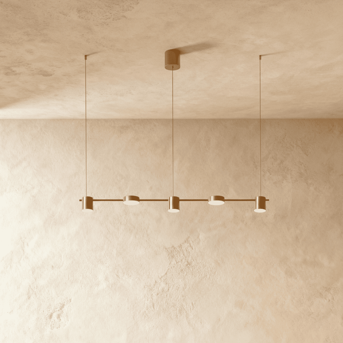 The Clérachic five-head pendant bar in brushed gold, its round LED heads glowing warm white against a plaster wall.