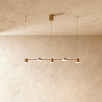 Angled view of the Clérachic gold five-head pendant bar, cylindrical heads glowing warm white beneath a textured ceiling.
