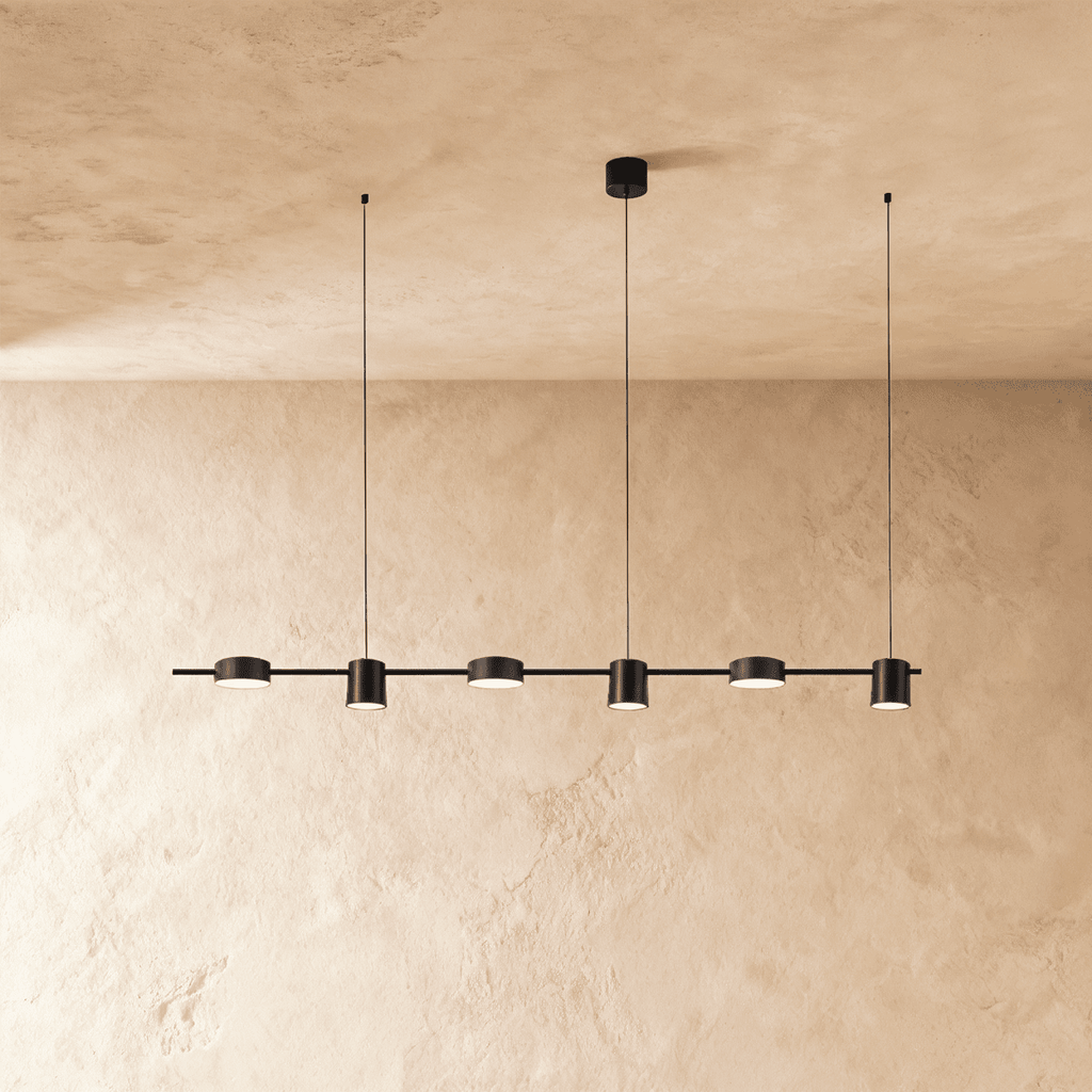Another angle of the Clérachic black six-head pendant bar, cylindrical heads glowing warm white on thin support cables.
