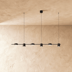 Another angle of the Clérachic black six-head pendant bar, cylindrical heads glowing warm white on thin support cables.