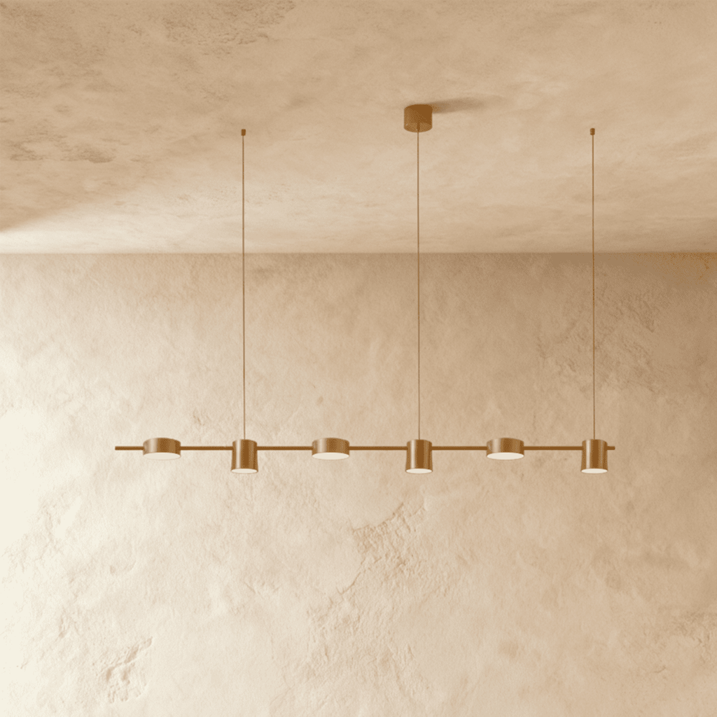 The Clérachic six-head pendant bar in brushed gold, its round LED heads glowing warm white against a plaster wall.