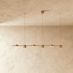 The Clérachic six-head pendant bar in brushed gold, its round LED heads glowing warm white against a plaster wall.