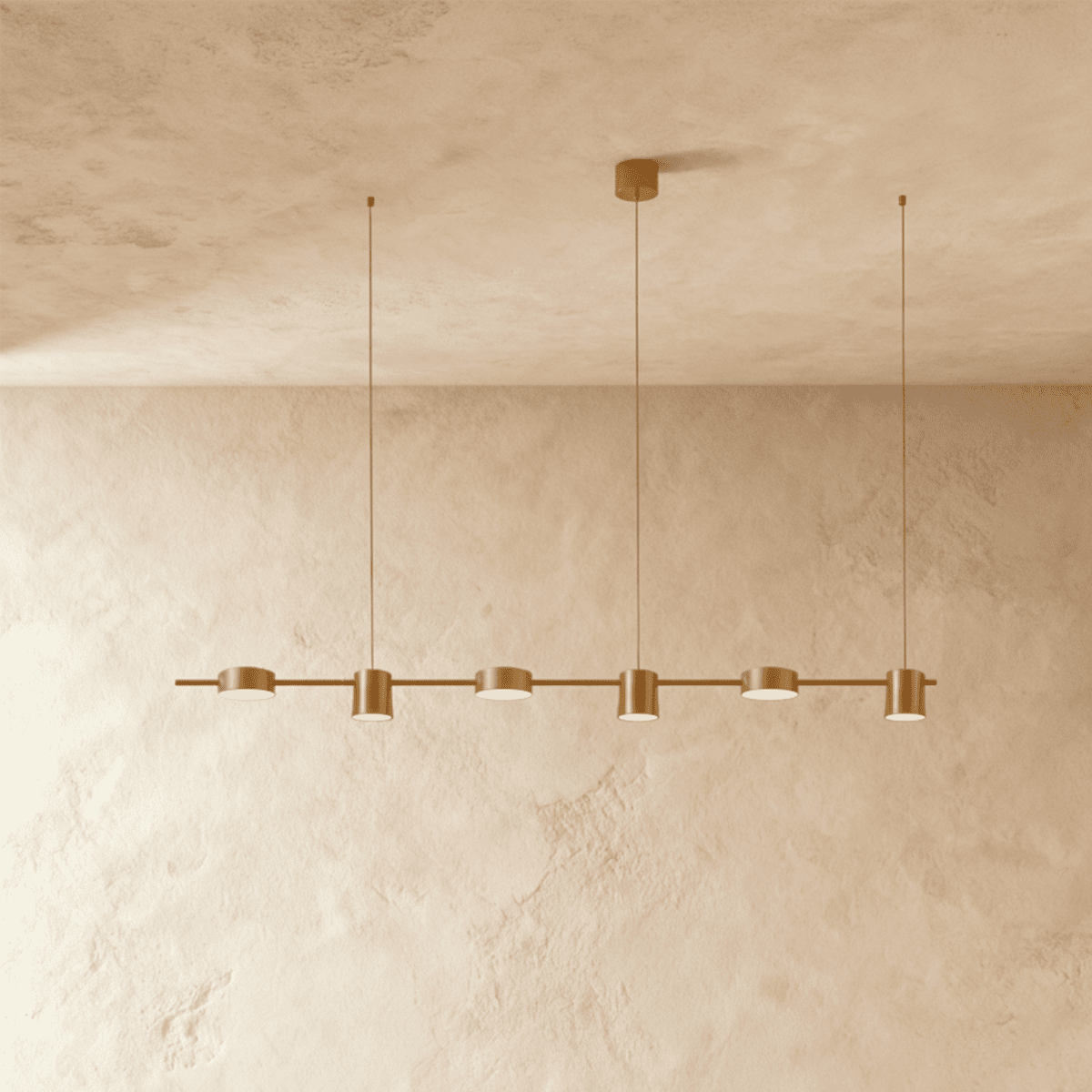 The Clérachic six-head pendant bar in brushed gold, its round LED heads glowing warm white against a plaster wall.