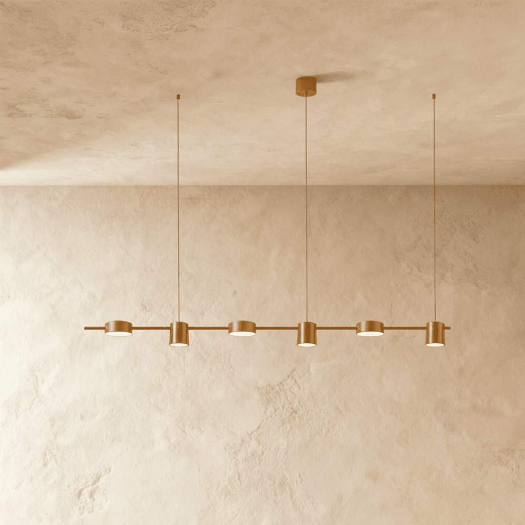 Close angle of the Clérachic gold six-head pendant bar, cylindrical heads glowing warm white beneath a textured ceiling.