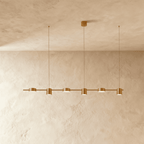 Close angle of the Clérachic gold six-head pendant bar, cylindrical heads glowing warm white beneath a textured ceiling.