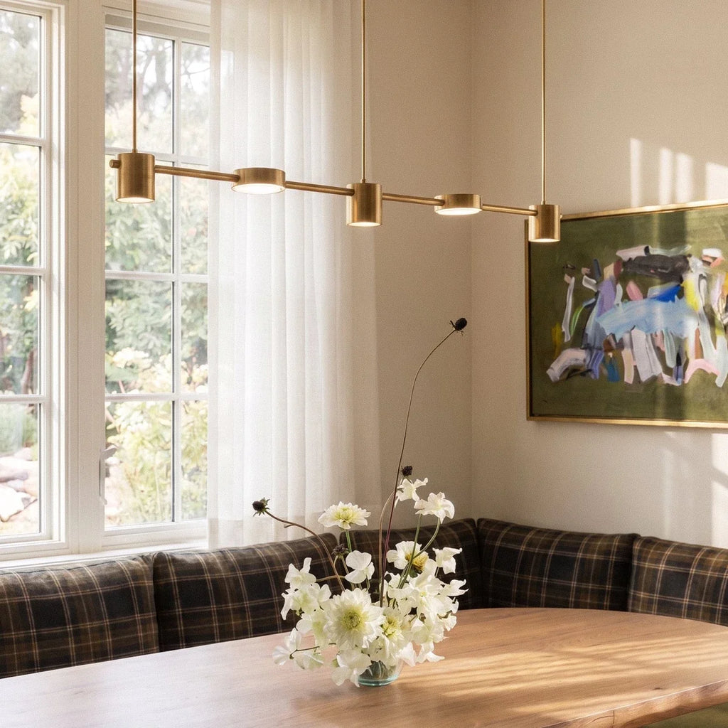 Close view of the Clérachic gold five-head pendant bar above a dining table set with white flowers near a garden window.