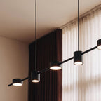 Close-up of the Clérachic black six-head pendant bar, its cylindrical heads glowing warm white against sheer curtains.