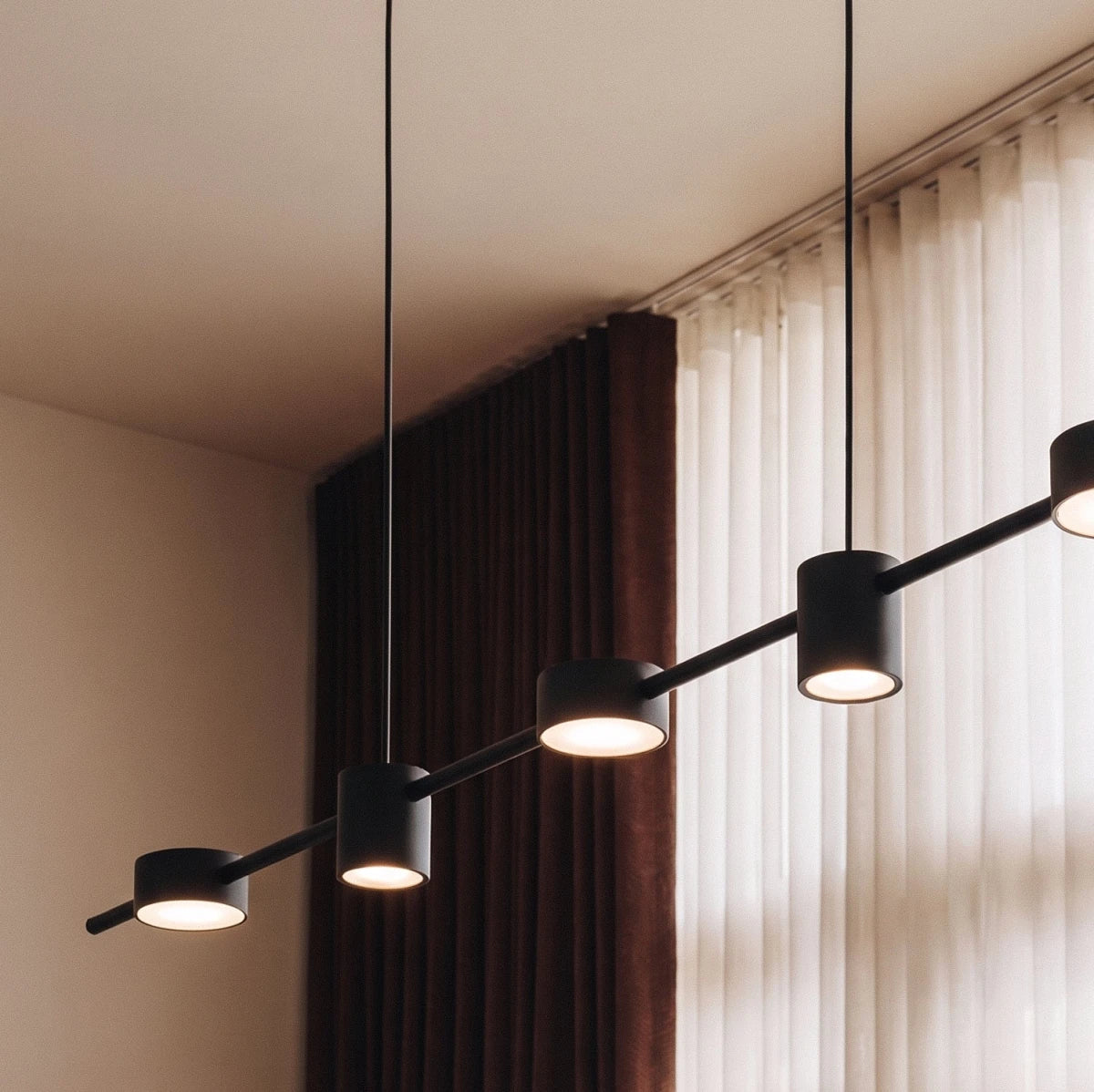 Close-up of the Clérachic black six-head pendant bar, its cylindrical heads glowing warm white against sheer curtains.