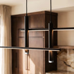 Close-up of a lit Clérachic black bar pendant light, its dual LED strips glowing warm above dark wood kitchen cabinets.