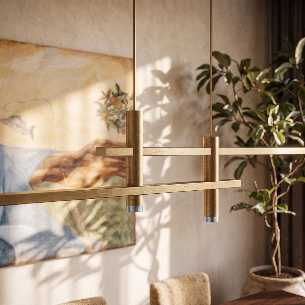 Close-up of an unlit Clérachic gold bar pendant light, its brushed brass bars catching afternoon light by a dining table.