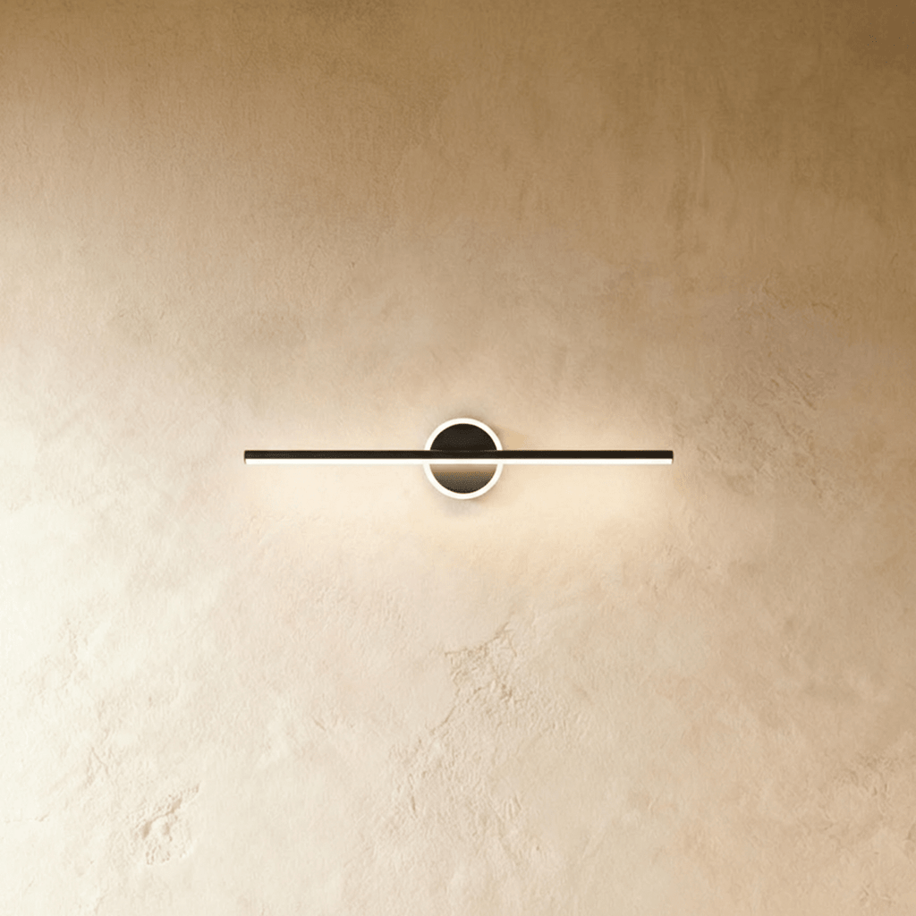 Clérachic slim black bar wall light crossing a round backplate with a glowing ring, shown on a warm limewash wall.