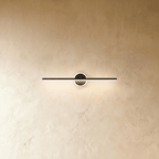 Clérachic slim black bar wall light crossing a round backplate with a glowing ring, shown on a warm limewash wall.