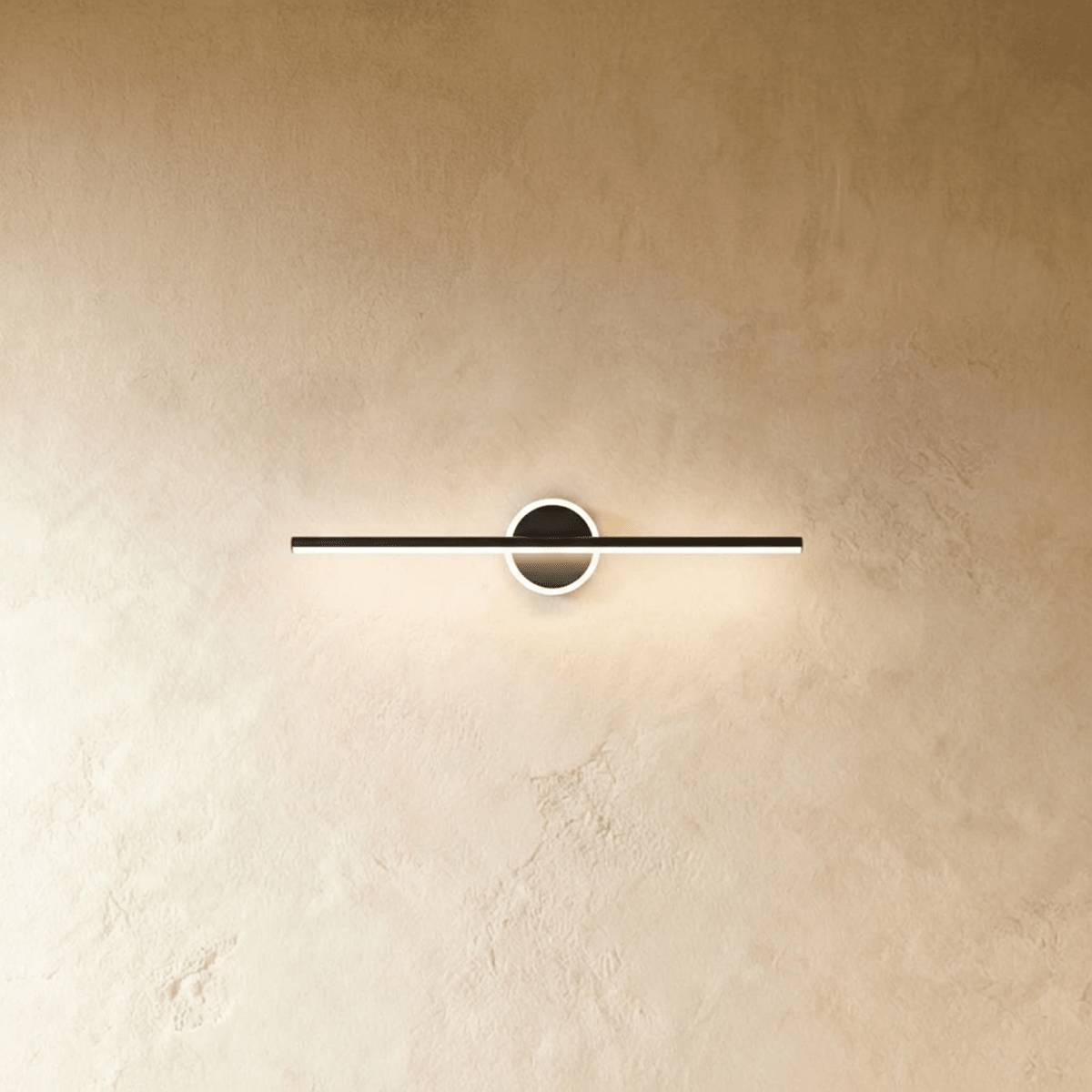 Clérachic slim black bar wall light crossing a round backplate with a glowing ring, shown on a warm limewash wall.