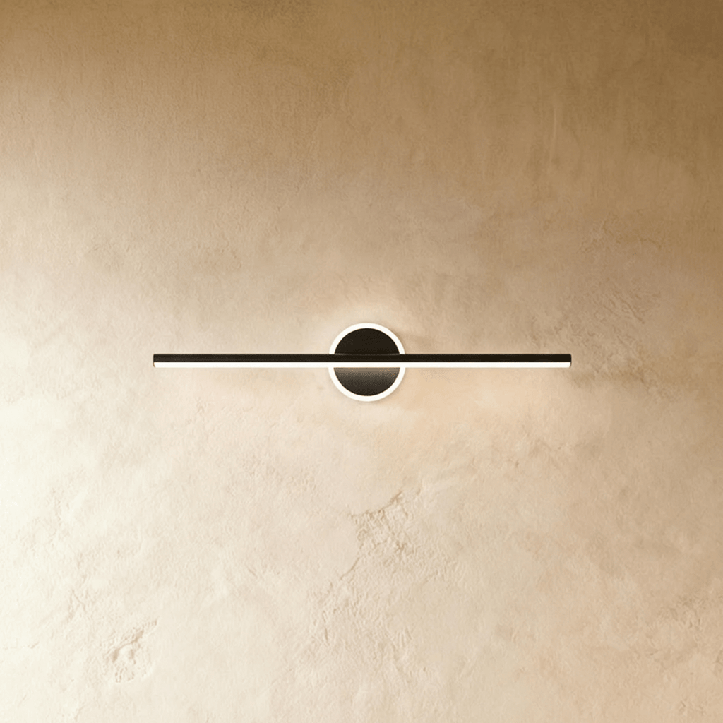 Clérachic longer black bar wall light with a lit ring backplate, mounted on a textured, warm cream plaster wall.