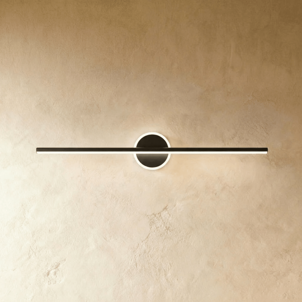 Clérachic longest black bar wall light with a glowing ring behind the bar, seen against warm textured plaster.