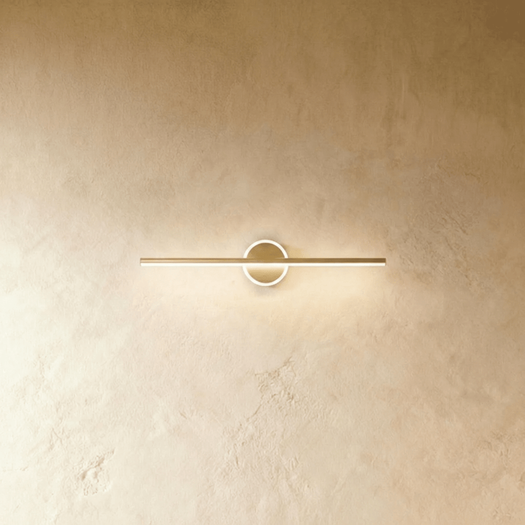 Clérachic slim gold bar wall light crossing a round backplate with a softly glowing ring on a limewash wall.