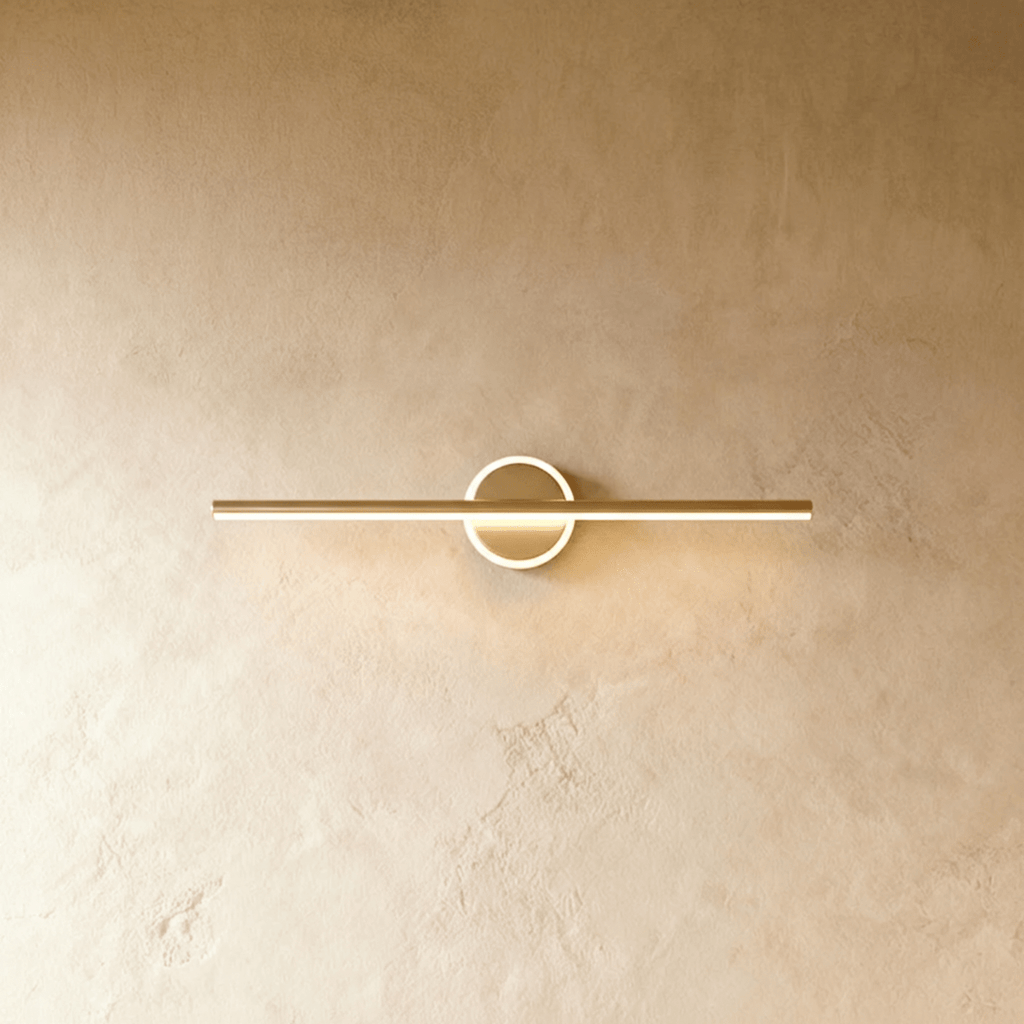 Clérachic longer gold bar wall light with a bright ring around its backplate, on a warm textured wall.